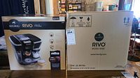 Two cardboard boxes side by side, left showing full product image, right plain box with Keurig Rivo branding