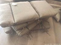 Stack of six light brown textured patio chair cushions with ties