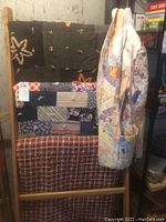 Photo showing three quilts with diverse patterns and a quilted blazer hanging.