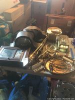 Photo showing a table covered with various vintage brass items including clocks, trays, a candle holder and framed pictures