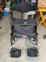 Front view of the foldable rollator/transport chair showing padded seat, backrest, footrests, and storage pouch.