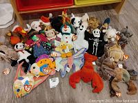 Photo showing a collection of assorted Beanie Babies plush toys laid out on floor, exhibiting variety of animals and characters, many with original Ty tags attached.