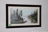 Framed and matted artwork showing cottage beside water, trees, and sailboats under calm sky.