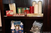 Display of assorted candles including pillar, taper, tealights, and battery-operated tealights along with UV3 branded furniture care bottles and cans on a dark wood shelf.