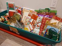 Top-down view of the storage tote filled with assorted Christmas gift wrapping supplies including ribbons, gift bags, cards, tags, and tissue paper.
