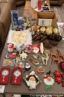 Table showing assorted Christmas ornaments including boxed ornaments, vintage glass Santa, various glass and glitter pieces laid out in groups.
