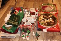 Overview of lot showing stacked textiles (towels, rugs), ceramic platters in boxes, salt and pepper shakers, party picks, and various small holiday items.