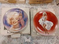 Two Marilyn Monroe collector plates on a fabric surface with their boxes partially visible.