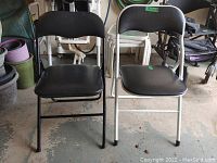 Front view of two folding chairs, black and white framed, on concrete floor.