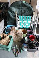 Photo showing lawn chair, synthetic shrub cover, several flower pots, decorative leaf garden ornament, gardening tools, and some small containers in crates on the ground.