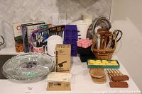Wide view of all kitchen items laid out including cookbook, swivel platter, kitchen tools, ice trays, and basket of utensils