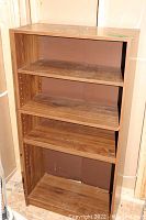 Front view of one laminate bookshelf, showing three shelves and brown wood grain laminate finish with surface wear.