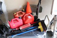 Photo showing three red gas cans, an orange plastic traffic cone, car brushes and scrapers inside a utility cart.