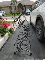 Full side view of the tall metal wine rack with visible leaf accents and six pairs of bottle holders.