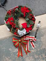 Top-down view of Christmas wreath in box with two decorative bows and a silver star over-the-door hanger, showing wreath decorations and item condition.