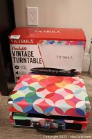 Photo showing the colorful geometric patterned Victrola portable turntable closed with the original box behind it.