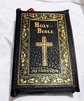 Front cover of the leather bound Holy Bible showing gold lettering and cross design with black leather texture.