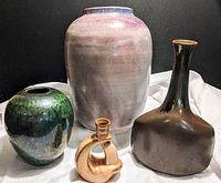 Four signed clay pots arranged on a cloth backdrop showing varied sizes and colors.