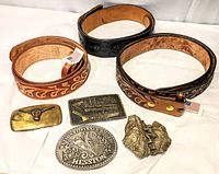Lot contents showing 3 hand-tooled leather belts and 4 belt buckles arranged on white background