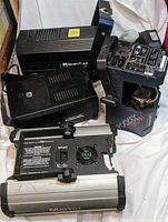 Four DJ lighting equipment pieces in a pile showing ventilation slots, control panels, and mounting hardware.