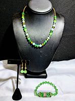 Necklace displayed on bust, earrings on stand, and bracelet laid flat showing design and colors