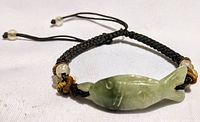 Jadeite koi fish centerpiece on black braided adjustable bracelet with two beads near ends, shown laying flat.