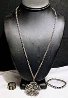 Full view of the necklace with floral pendant and two rhinestone bracelets displayed on a black stand.