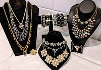 Full overview of 18-piece rhinestone jewelry lot on black display busts and bracelet holder