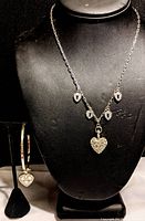Photo of necklace displayed on black bust featuring silver-tone chain with five heart-shaped rhinestone charms, including a larger heart pendant.