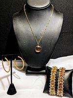 Full view of two bracelets, necklace with pendant on display bust, and hoop earrings on stand