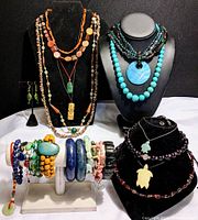 Full lot arrangement showing a variety of semi-precious stone jewelry pieces including necklaces, bracelets, and earrings displayed on black and white stands.