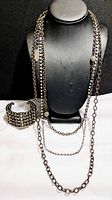 Full view of multi-strand silver-tone long chain necklace displayed on bust and matching wide silver-tone cuff bracelet with rhinestones on white surface.