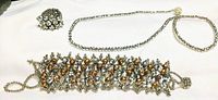 Multi-row rhinestone bracelet, silver-tone chain necklace, and ring laid out on white fabric