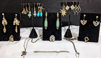 Full lot photo showing 9 pairs of earrings displayed on black stands, 3 pendants on necklaces, and a bracelet laid out in front