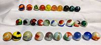 Full collection of 30 colorful vintage glass marbles arranged in three rows to show variety of colors and swirl patterns