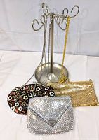 Three vintage purses hanging on metal display stand: one floral embroidered fabric purse, one small silver-tone mesh purse with chain, and one medium gold-tone mesh purse with chain.