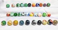 Multiple rows of vintage glass marbles with various colors and swirl patterns on a white cloth background
