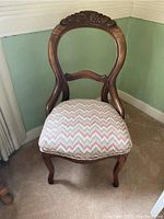 Front view of one of the antique chairs showing carved wooden backrest and herringbone patterned upholstery on the seat.