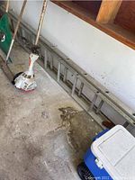 Photo showing the aluminum extension ladder resting horizontally against a wall on the garage floor beside small tools.