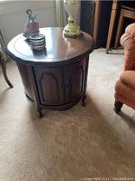 Photo of closed round dark walnut side table with decorative molding and items on top.