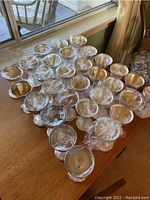 26 silver plated Birks goblets arranged on a wooden table, most covered with plastic wrap.