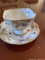 Front view of one tea cup seated on its saucer showing scalloped rim, floral sprays and gold gilt edge