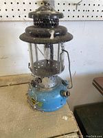 Front three-quarter view of Sears gas lantern showing blue fuel tank, glass globe and black ventilator cap