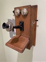 Front and side view of antique wooden wall-mounted telephone showing bells, mouthpiece, and crank handle