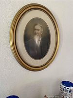 Full view of the antique oval framed photograph hung on a textured white wall.