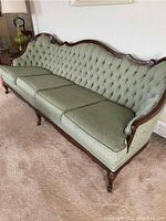 Front and side view of the antique walnut sofa showing green tufted upholstery and carved wooden frame.