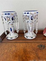 Pair of white and blue glass lustres on wood surface