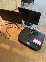 Photo showing two black computer monitors and HP Envy 5010 all-in-one scanner/printer on carpeted floor