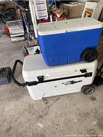 Photo of blue Coleman cooler on top of larger white Igloo cooler, both with wheels and lids.