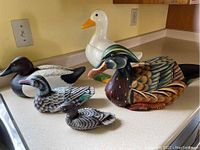 All five items positioned on a kitchen counter: one ceramic goose cookie jar and four wooden ducks including the wine bottle holder.